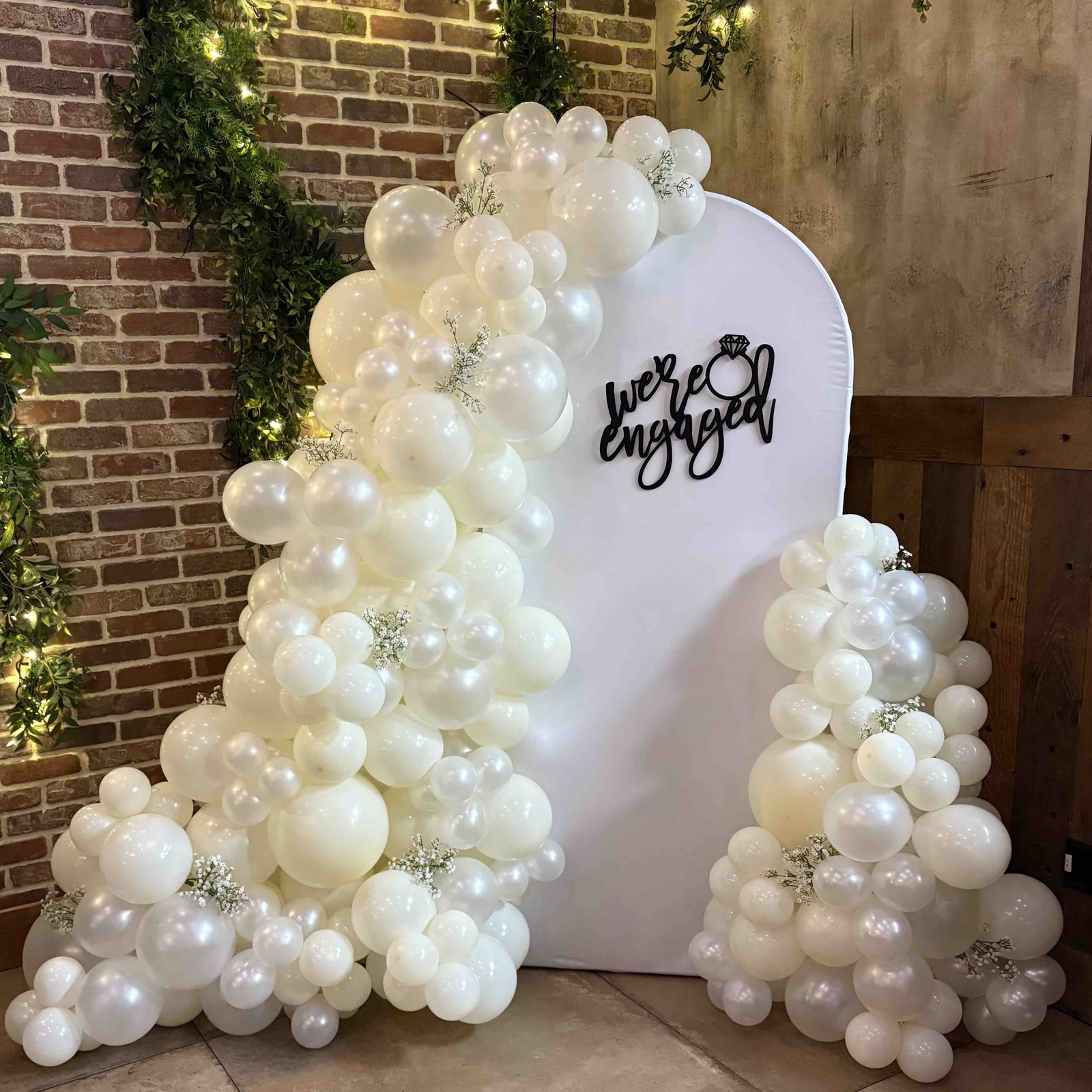 Organic white balloon arch installed on a brick backdrop for an engagement soirée in Morris County, NJ